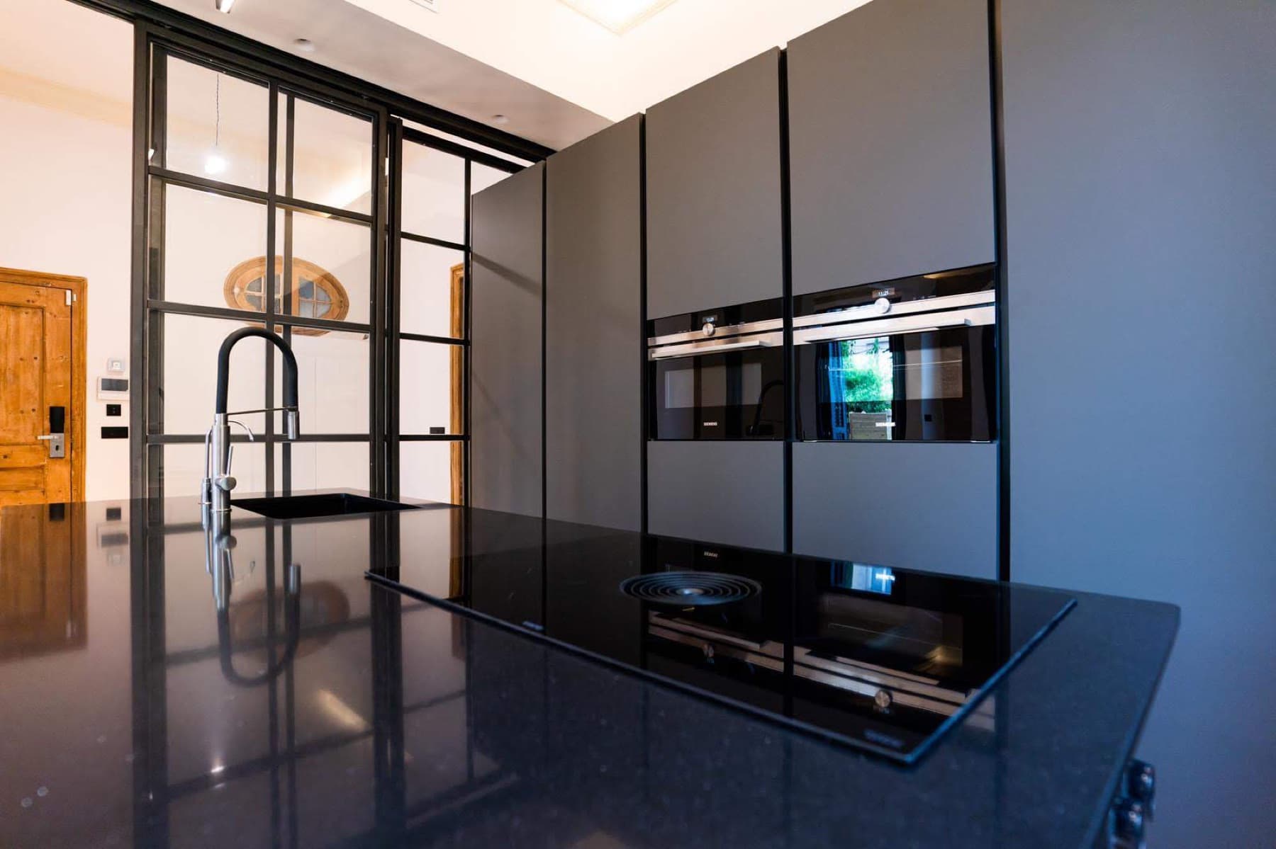 Cocina reformada en Barcelona con isla negra y cerramiento de cristal tipo industrial